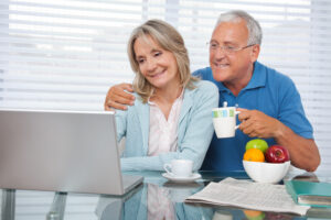 Happy older couple using laptop while having breakfast